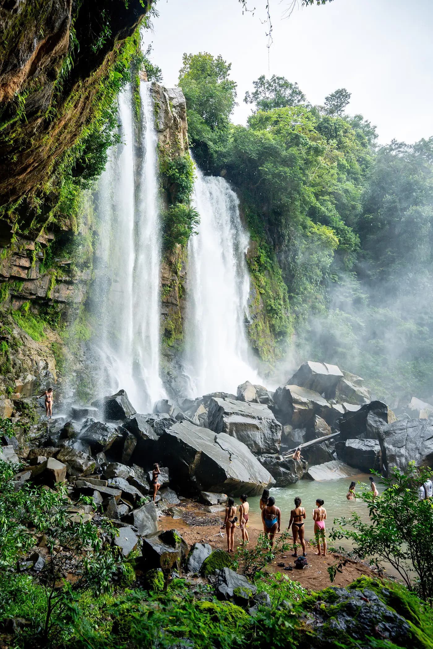 Guests from Vajra Jahra Retreat Center exploring behind a majestic tropical waterfall surrounded by lush greenery.