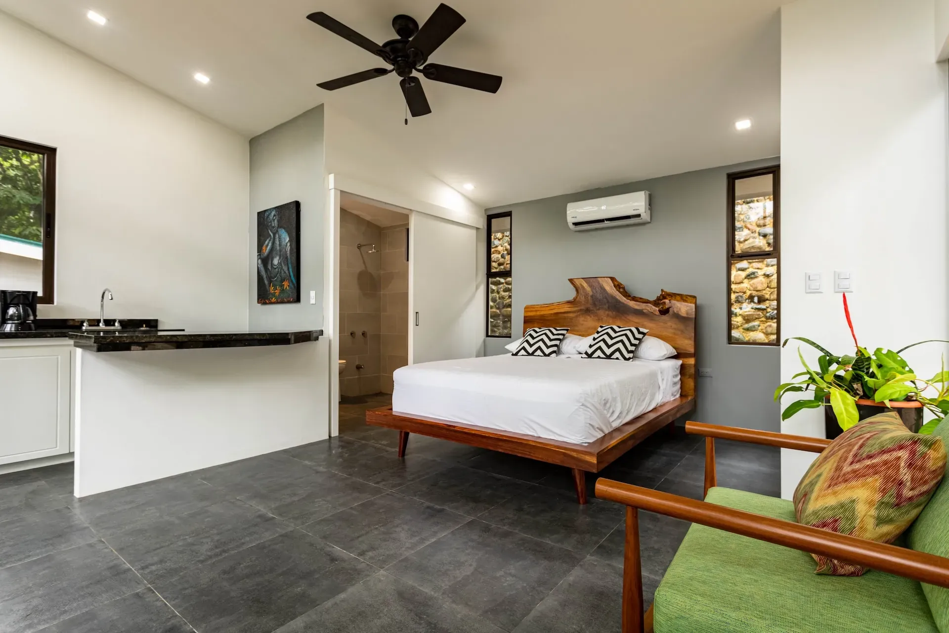 Modern villa room with wood bed, kitchenette, and green chair at Vajra Jahra Retreat Center in Costa Rica.
