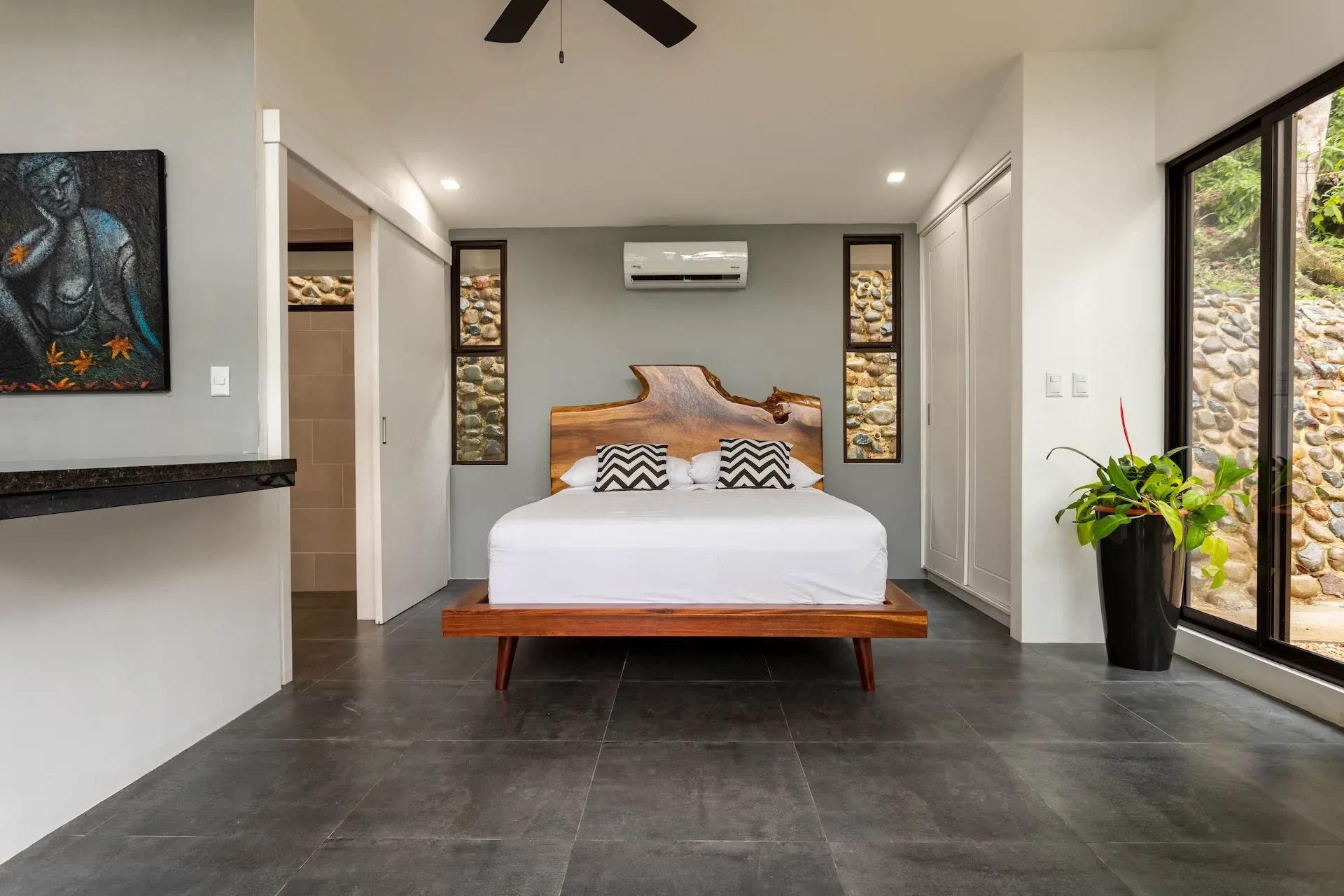 Villa bedroom with natural wood headboard, stone wall accents, and large windows at Vajra Jahra in Costa Rica.