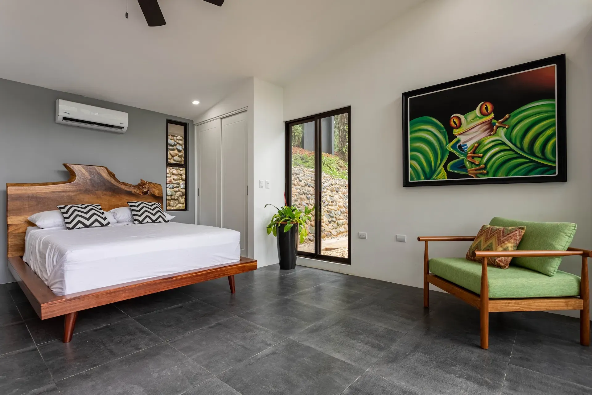 Villa bedroom with wood bed frame, green lounge chair, and frog artwork at Vajra Jahra in Costa Rica.