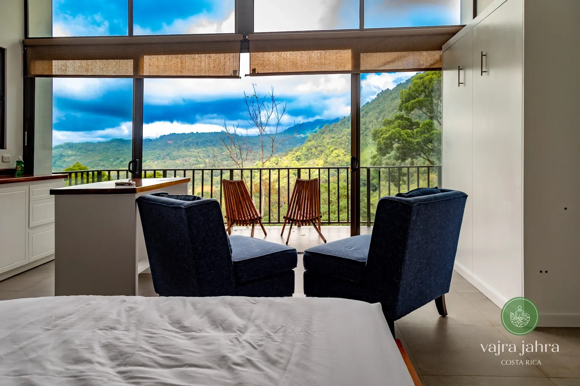 Upper villa interior with two chairs and a mountain view through glass doors at Vajra Jahra Retreat Center.