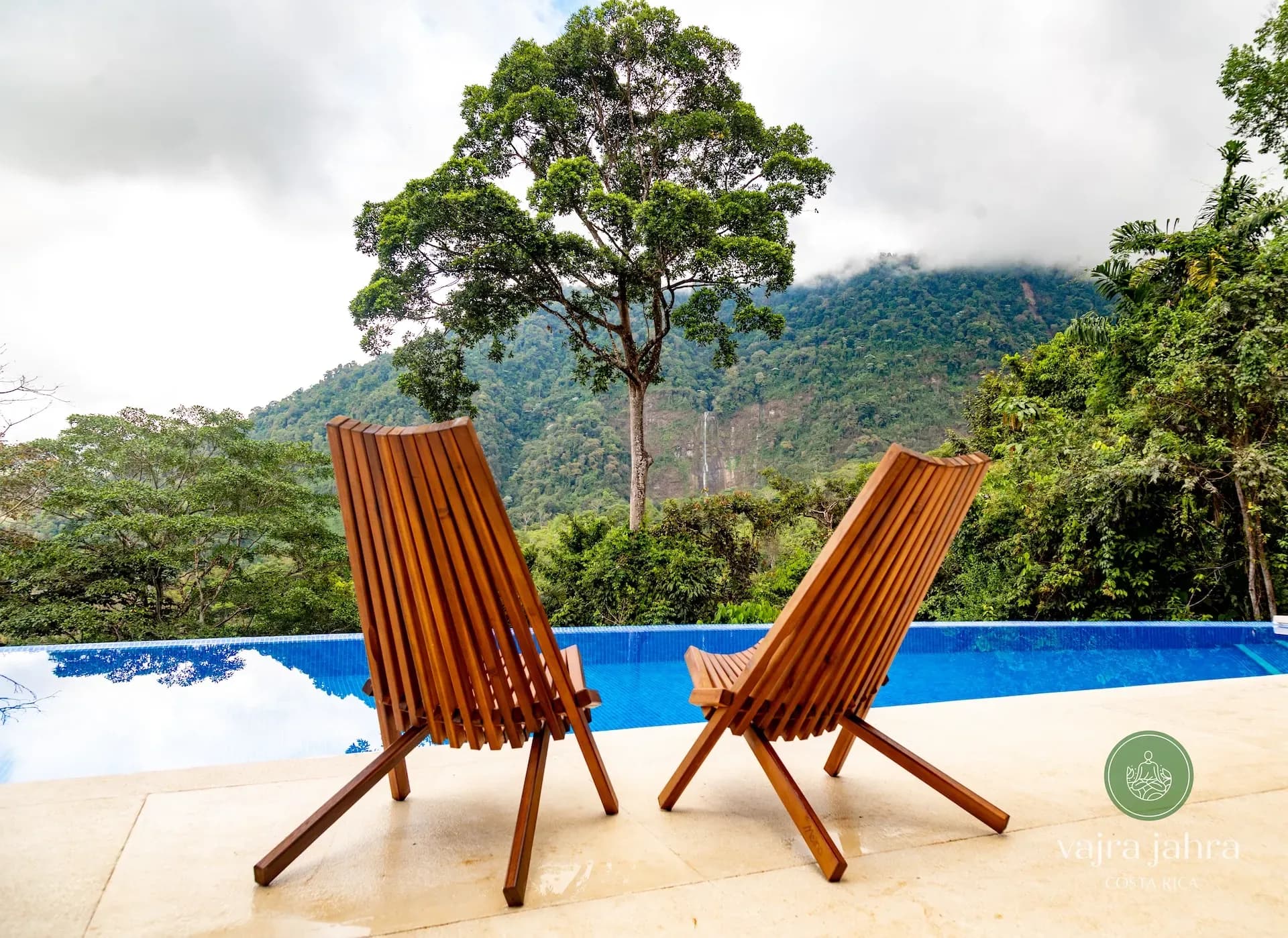 Chairs on the deck of Vajra Jahra's pool, a perfect place to relax on a wellness retreat and take in jungle views.