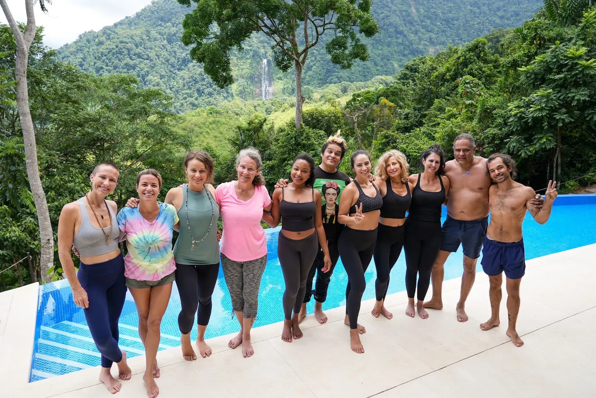 Vajra Jahra retreat-goers smiling in front of the infinity pool, with the towering Diamante Waterfall in the distance.