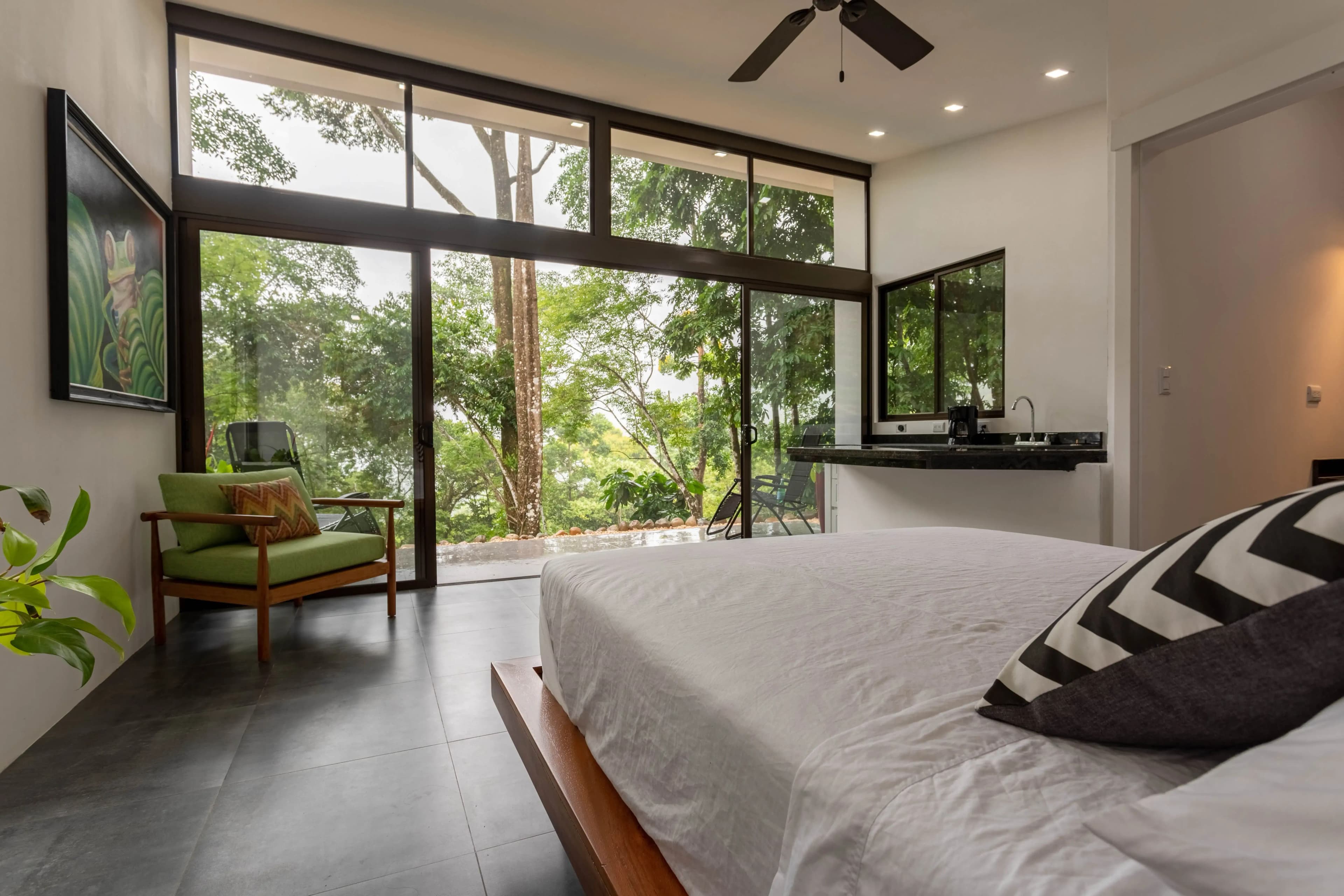 One of the villas interiors of the retreat venue, featuring floor to ceiling windows with jungle views. Villa is equipped with queen bed and small seating area.