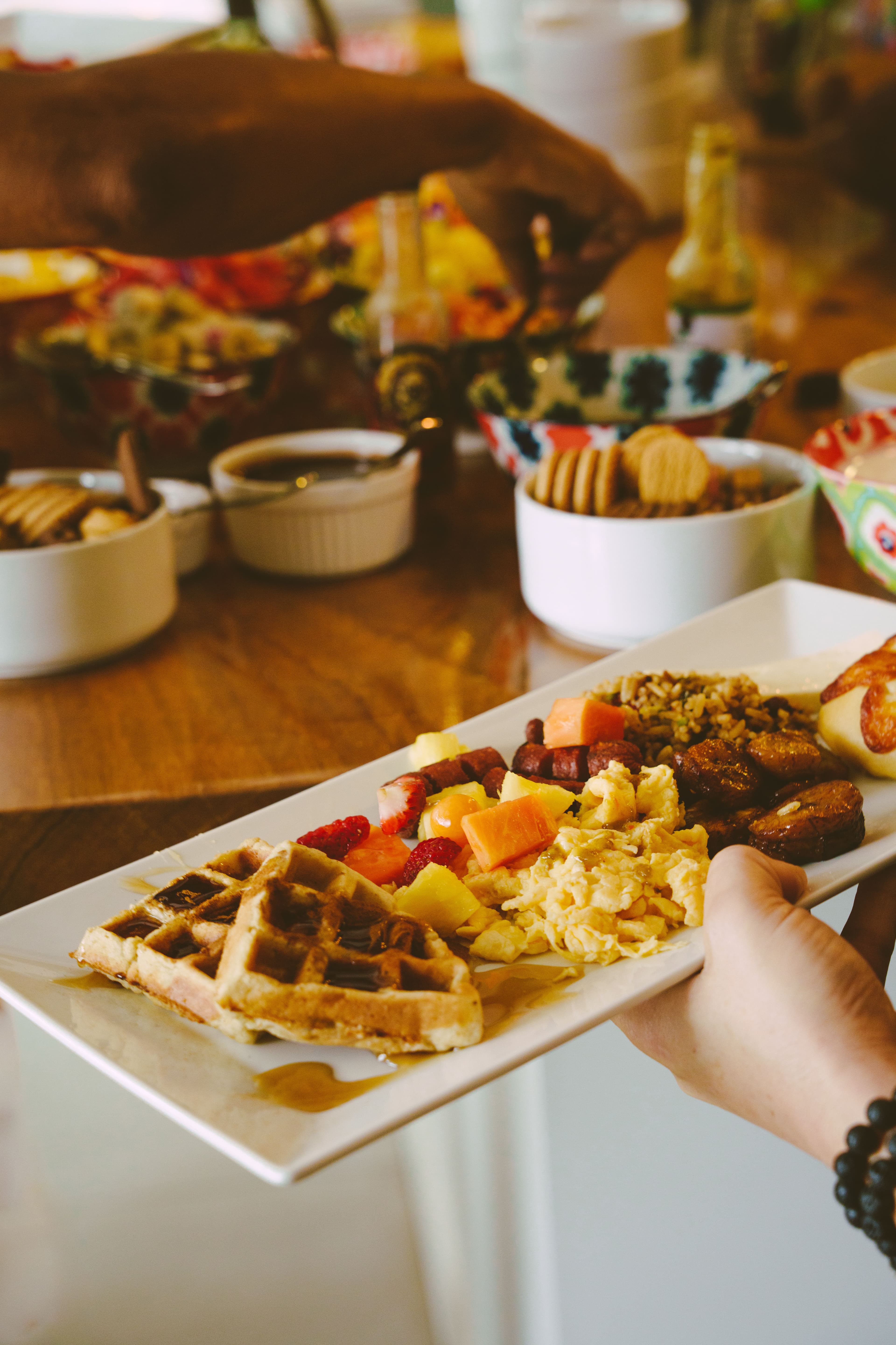 A retreat guest holding a plate of breakfast foods including waffles, eggs, fruits, and other local foods.
