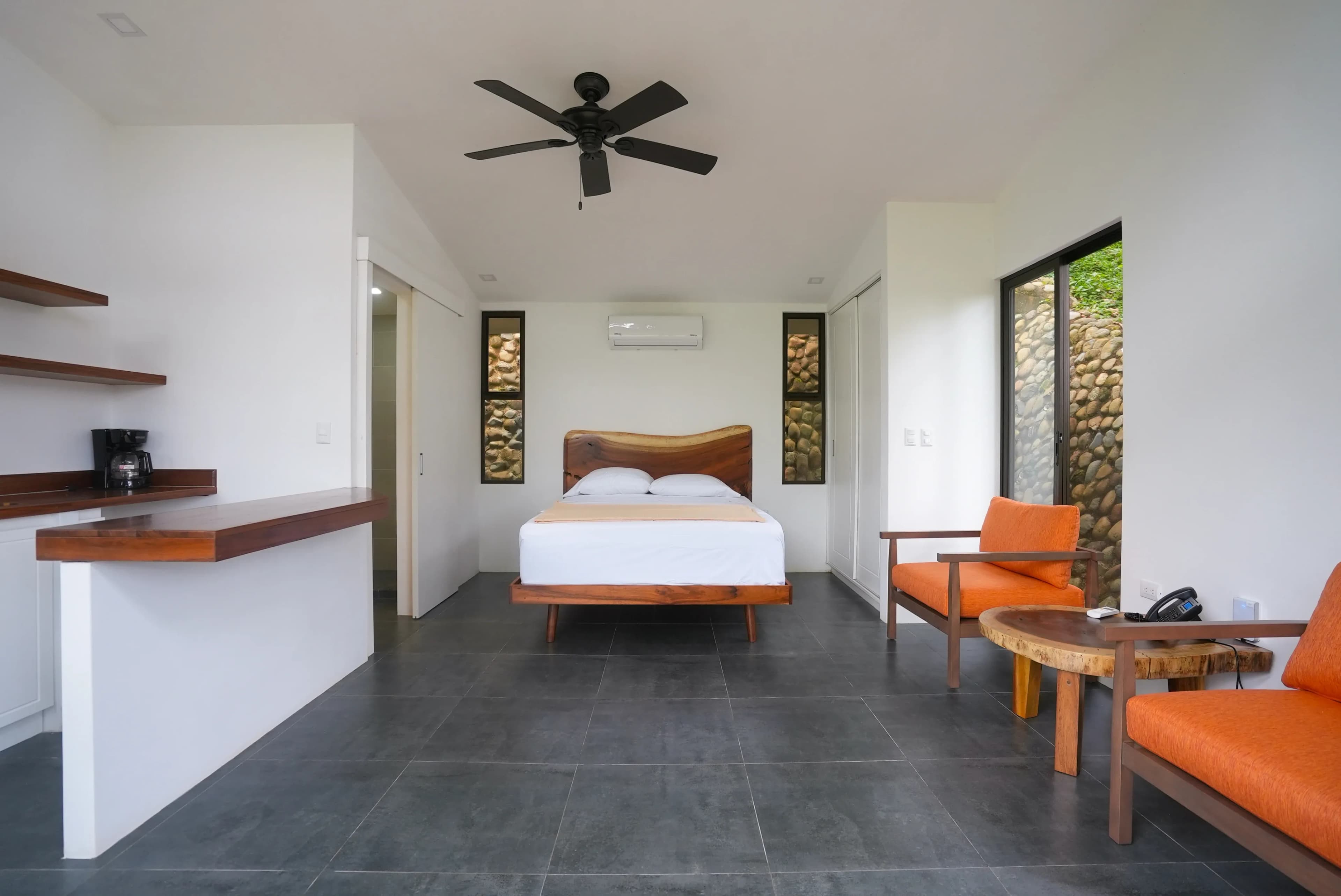 Interior view of one of the villas with a queen bed, two chairs, small kitchen, and bathroom.