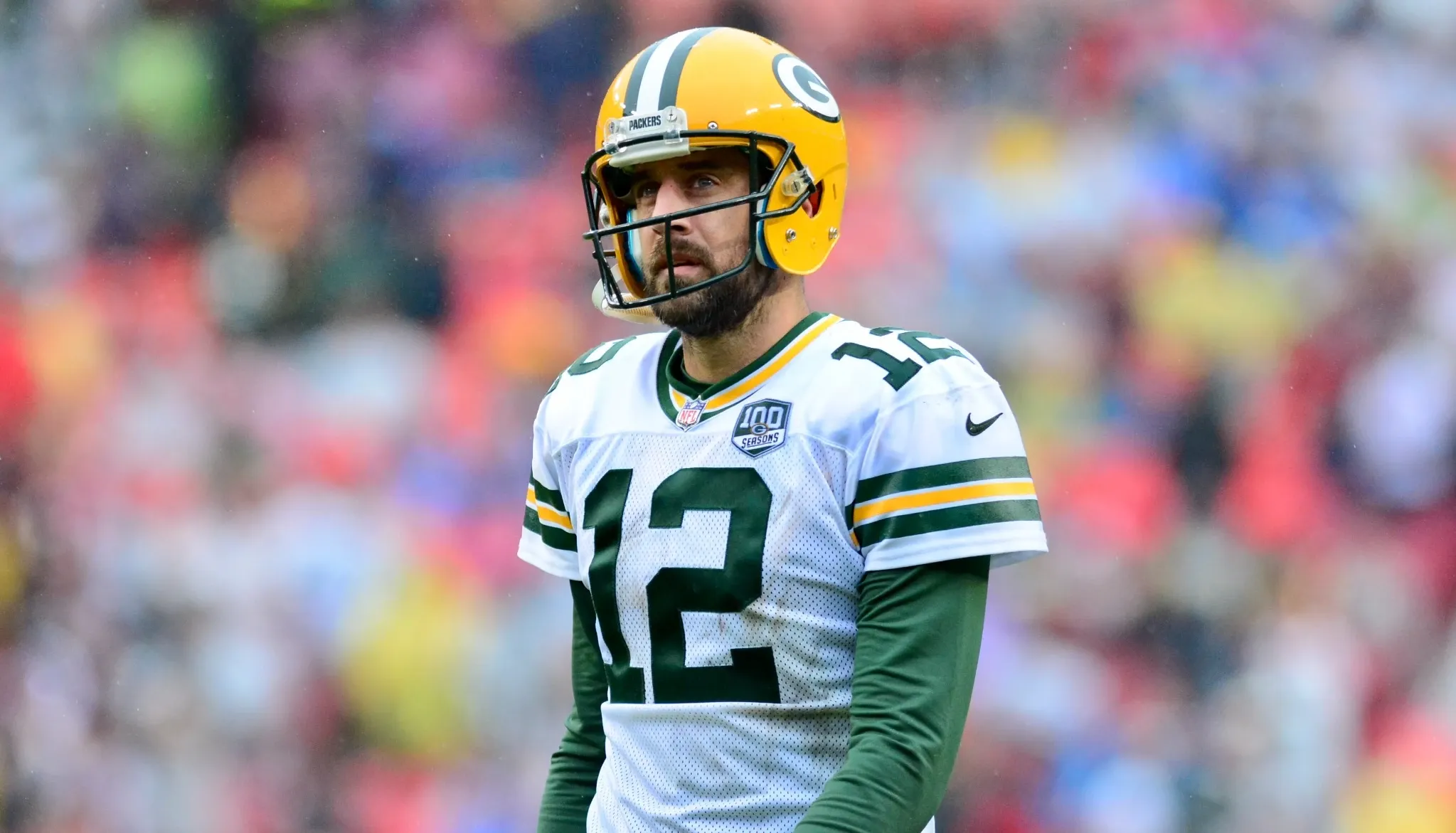 Aaron Rodgers in full Green Bay Packers uniform with a large crowd blurred out in the background.