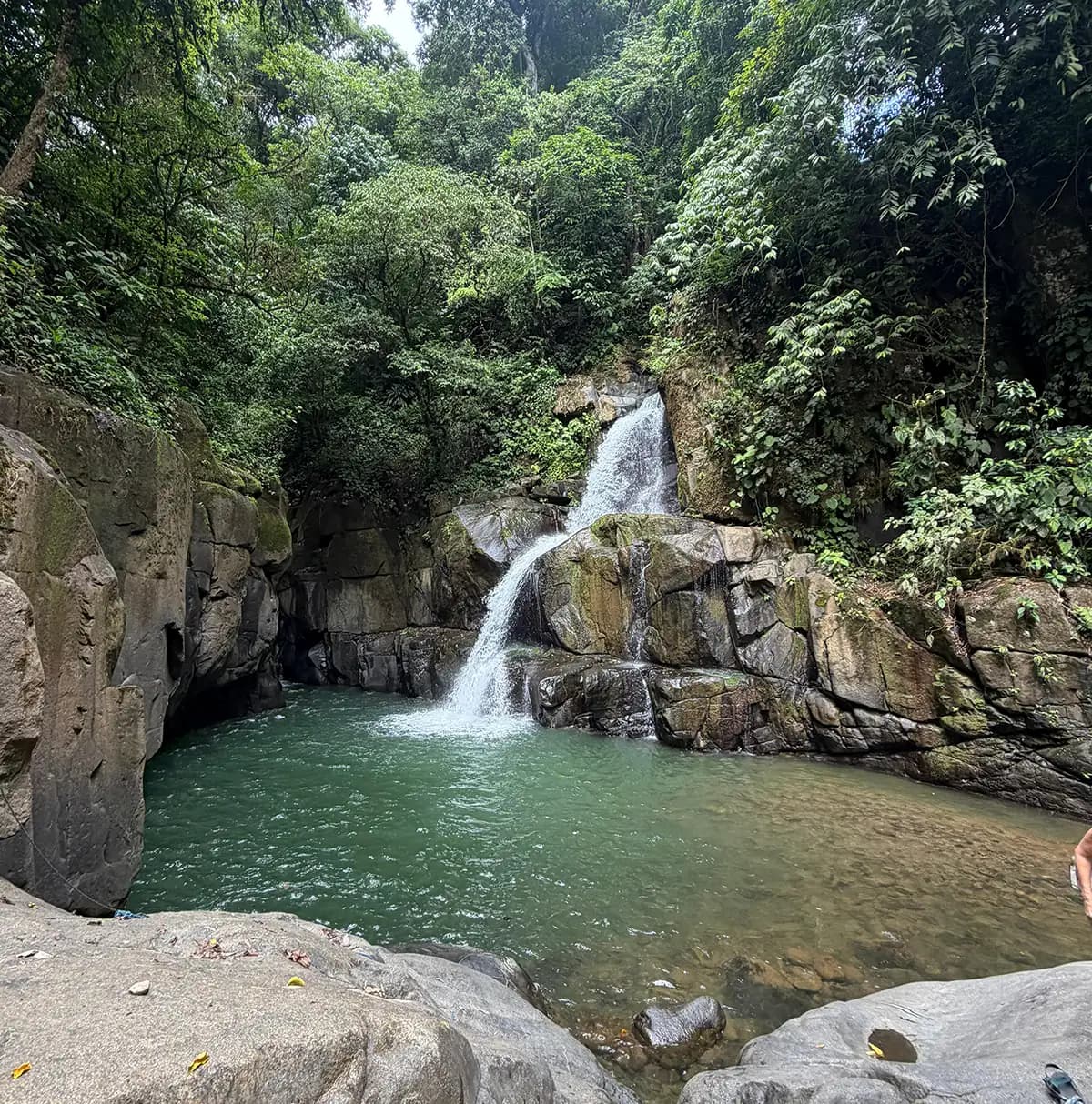 Scenic waterfall flowing into a natural pool surrounded by lush tropical greenery near Vajra Jahra.