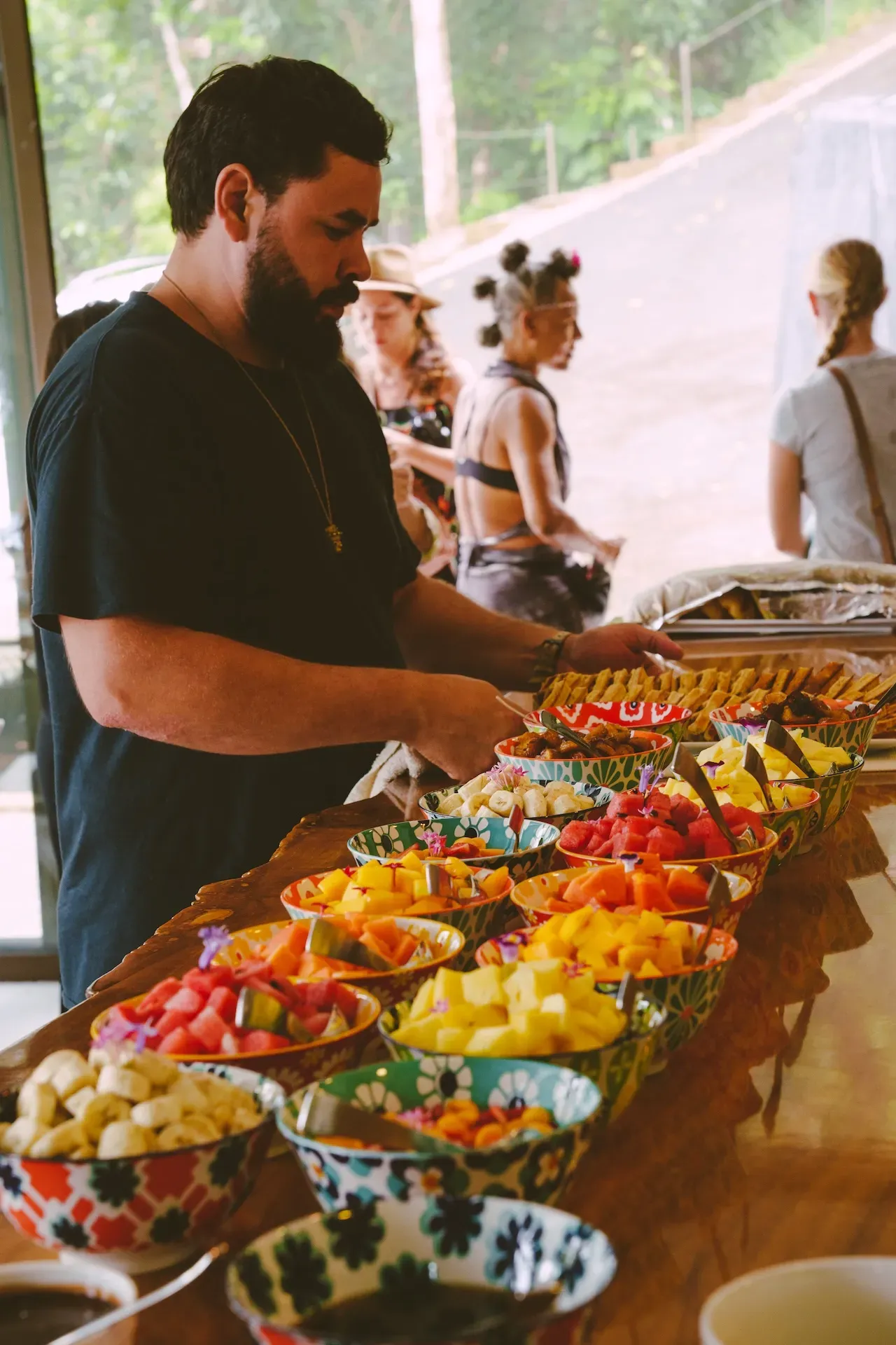 A guest selecting fresh tropical fruits from a colorful buffet at a Costa Rica Retreat Center, highlighting the vibrant dining experience at Vajra Jahra.