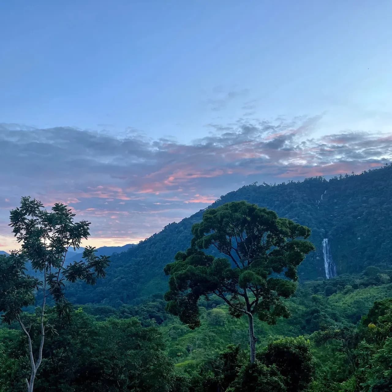 Morning sky over lush mountains and a distant waterfall near Vajra Jahra, a serene Costa Rica Retreat Center immersed in jungle beauty.