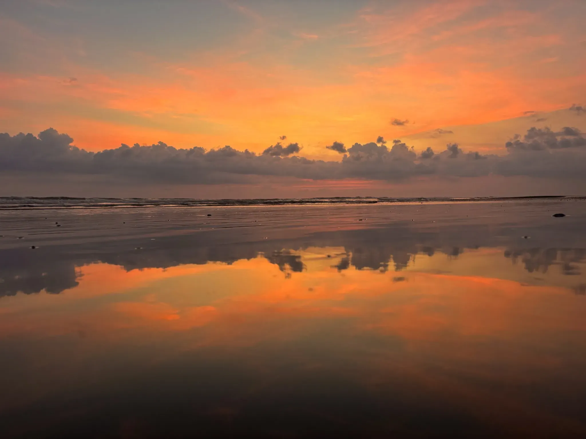 A glowing orange sunset reflecting over a calm shoreline at a serene beach near the Costa Rica Retreat Center, capturing the peaceful atmosphere of Vajra Jahra.