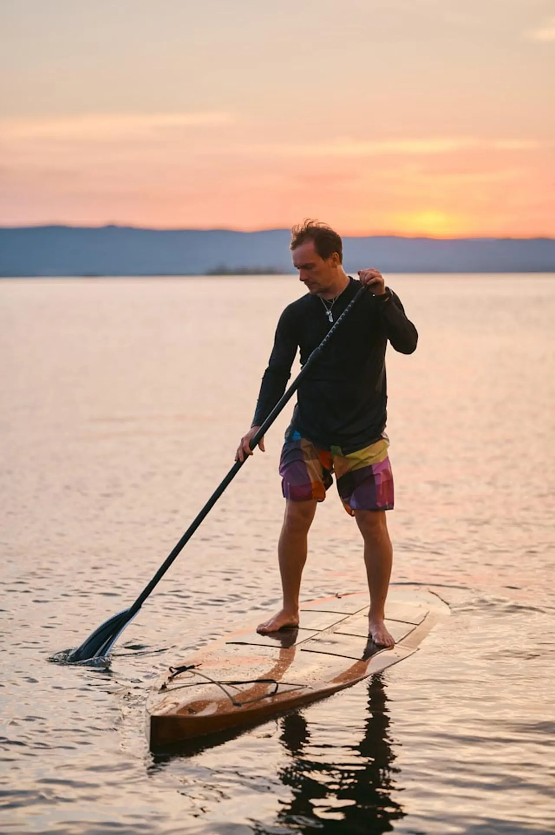 Man paddleboarding on calm waters near Vajra Jahra Retreat Center, offering a serene experience for anyone choosing to rent a retreat center.