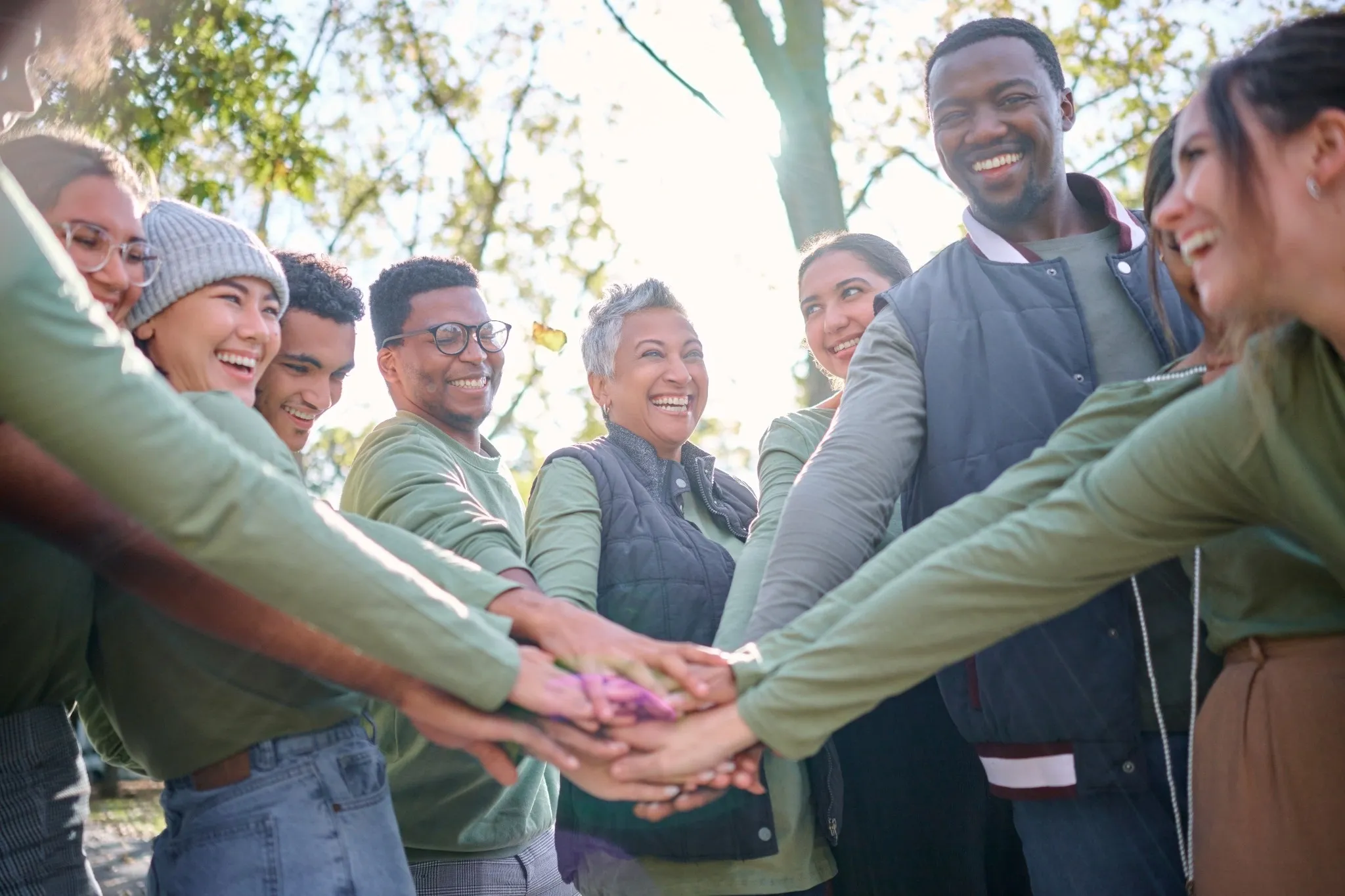 A circle of team members putting their hands together to signify teamwork during an outdoor business retreat, preparing for team building retreat activities.