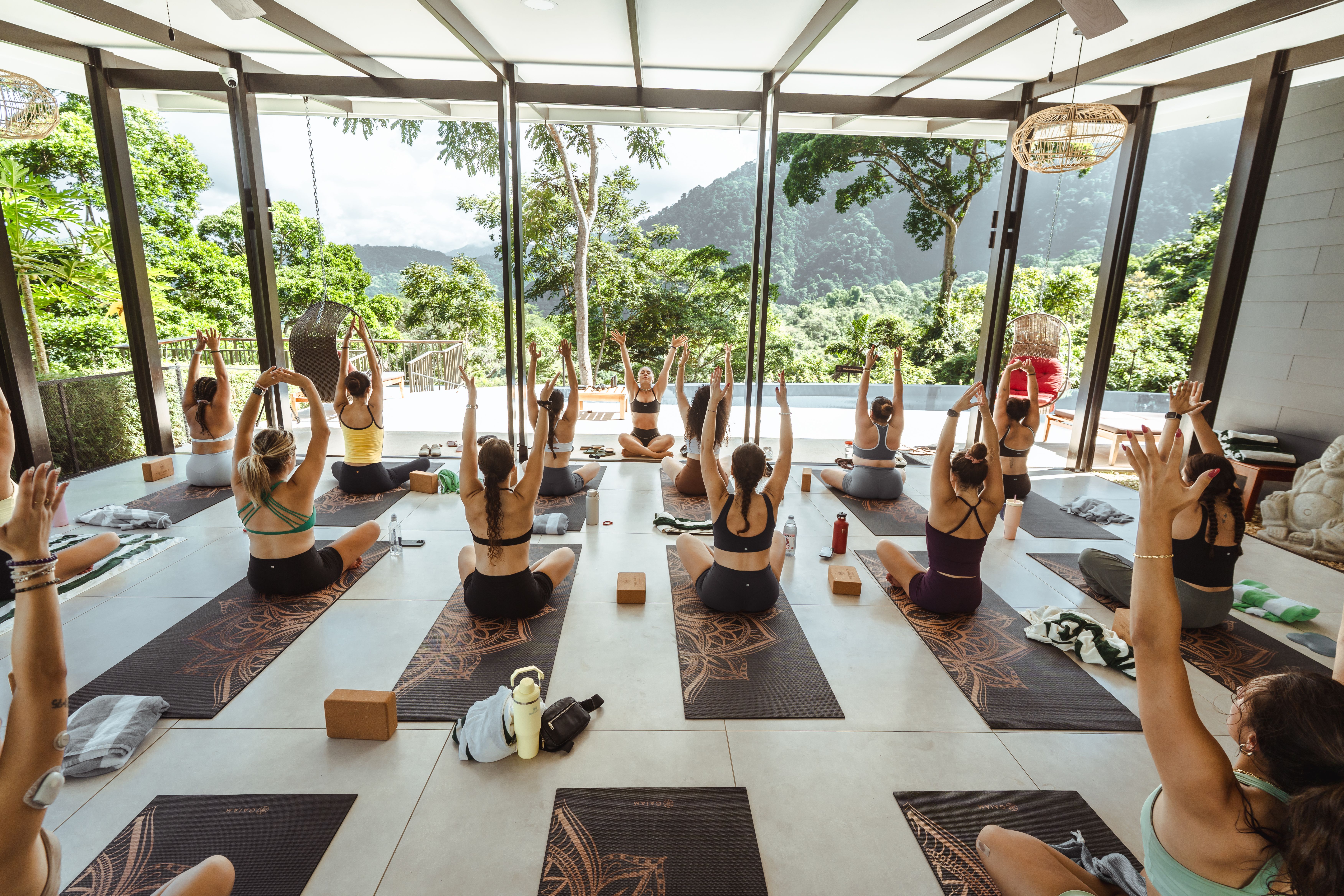 An instructor practicing yoga with trainees in an open air yoga studio, sharing the benefits of yoga teacher training.