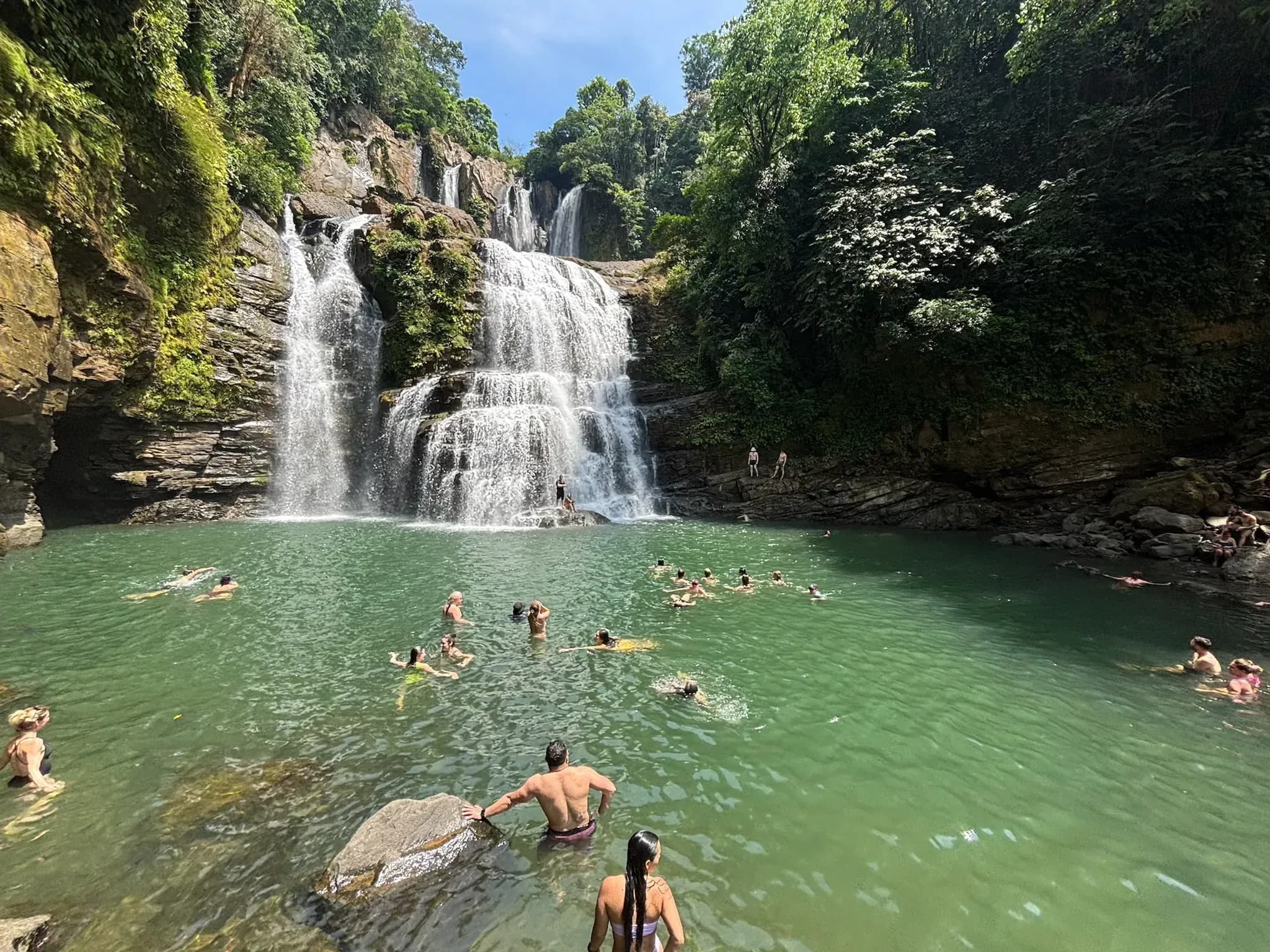 Guests swimming beneath a tropical waterfall surrounded by lush greenery near Vajra Jahra Retreat Center, enjoying a rejuvenating retreat Costa Rica adventure.