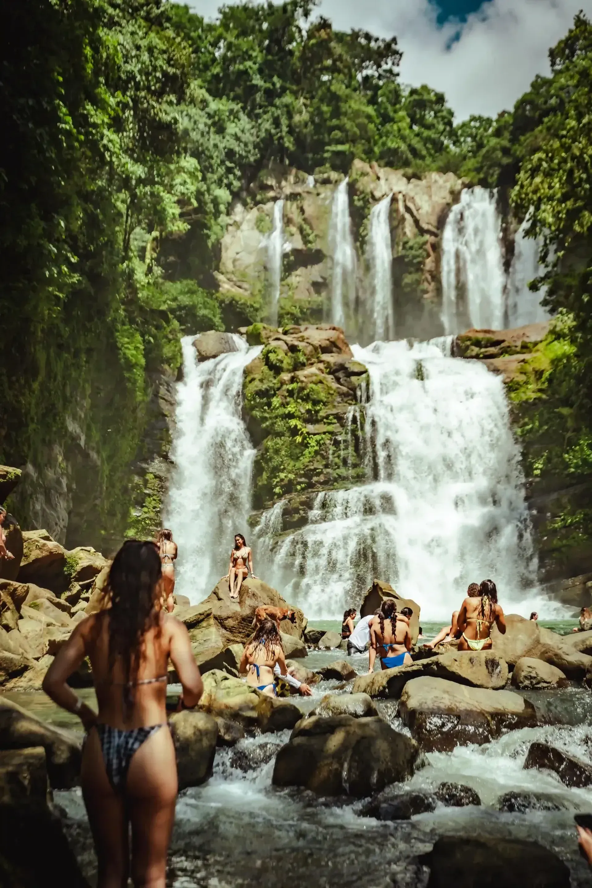 People relaxing and exploring at a lush multi-tier waterfall in Costa Rica, showcasing an immersive nature experience near Vajra Jahra Retreat Center for Costa Rica Yoga Teacher Training participants.