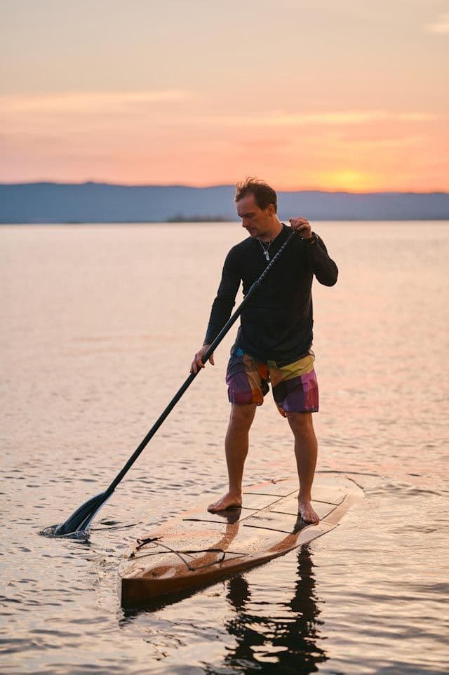 Man paddleboarding during a golden sunset, part of San Jose Costa Rica Excursions available through Vajra Jahra Retreat Center.