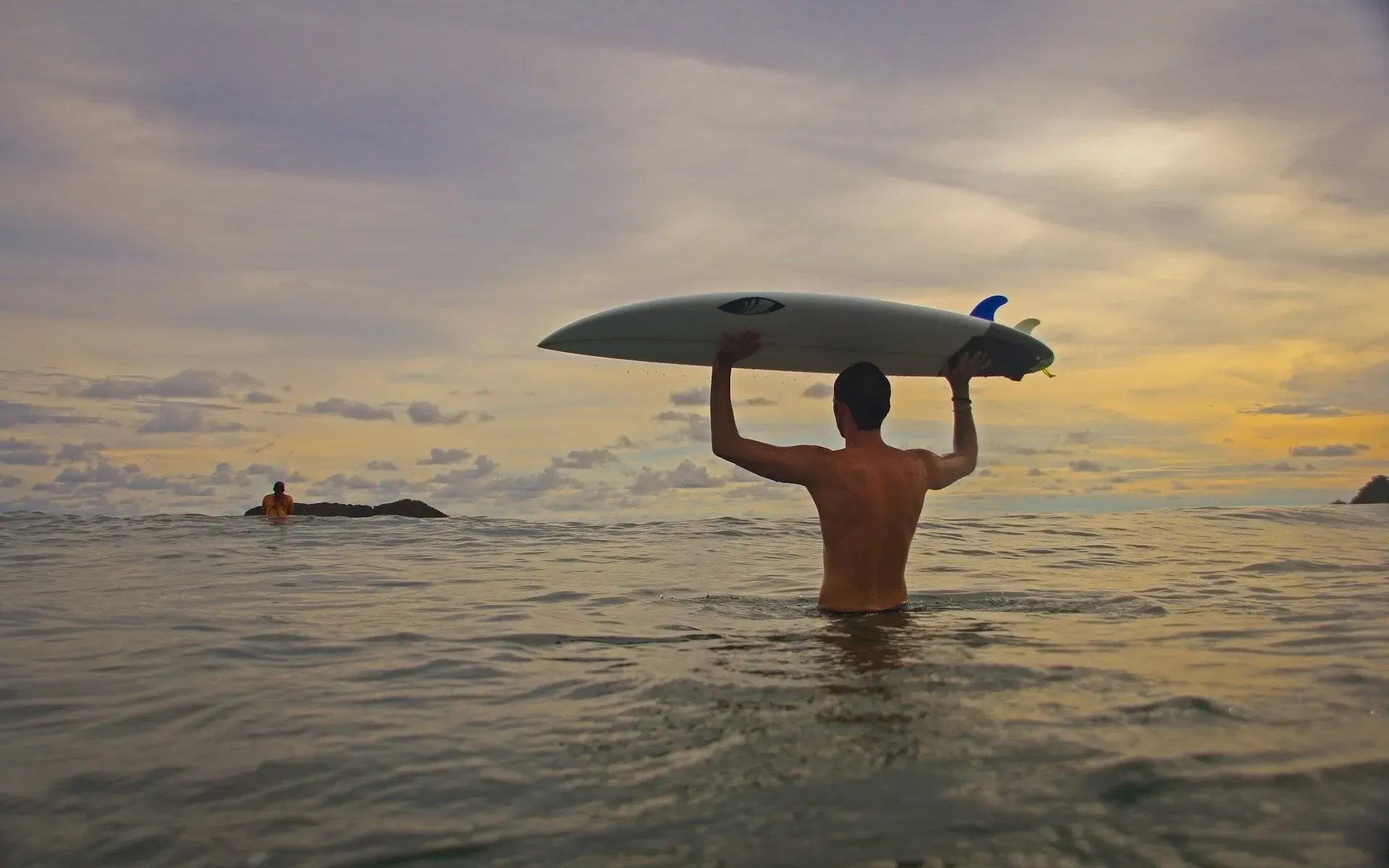 Surfer holding a board above the water during a sunset session offered by Vajra Jahra Wellness Retreat Center.